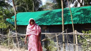 Women in front of her houses who received roof sheet from YPSA
